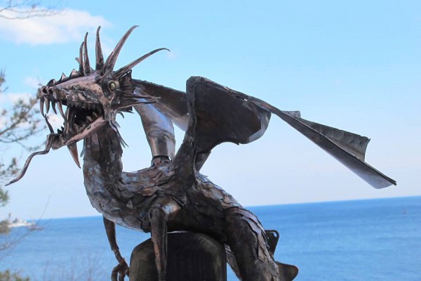 copper sculpture of dragon outside in front of ocean